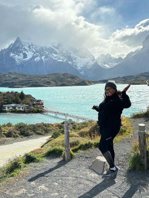 a person poses in front of mountains and water